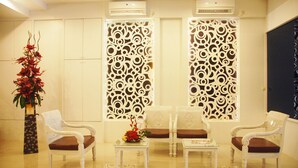 A reception area with two white armchairs, a small table with a vase of flowers, and decorative panels with circular patterns. - Gandhi Inn (Medan)