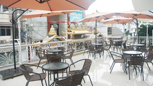 An outdoor cafe area with tables and chairs, umbrellas, and a decorative railing. - Gandhi Inn (Medan)