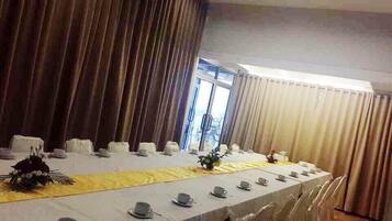 A conference room with a long table set for a meeting, surrounded by chairs, and large curtains on either side.