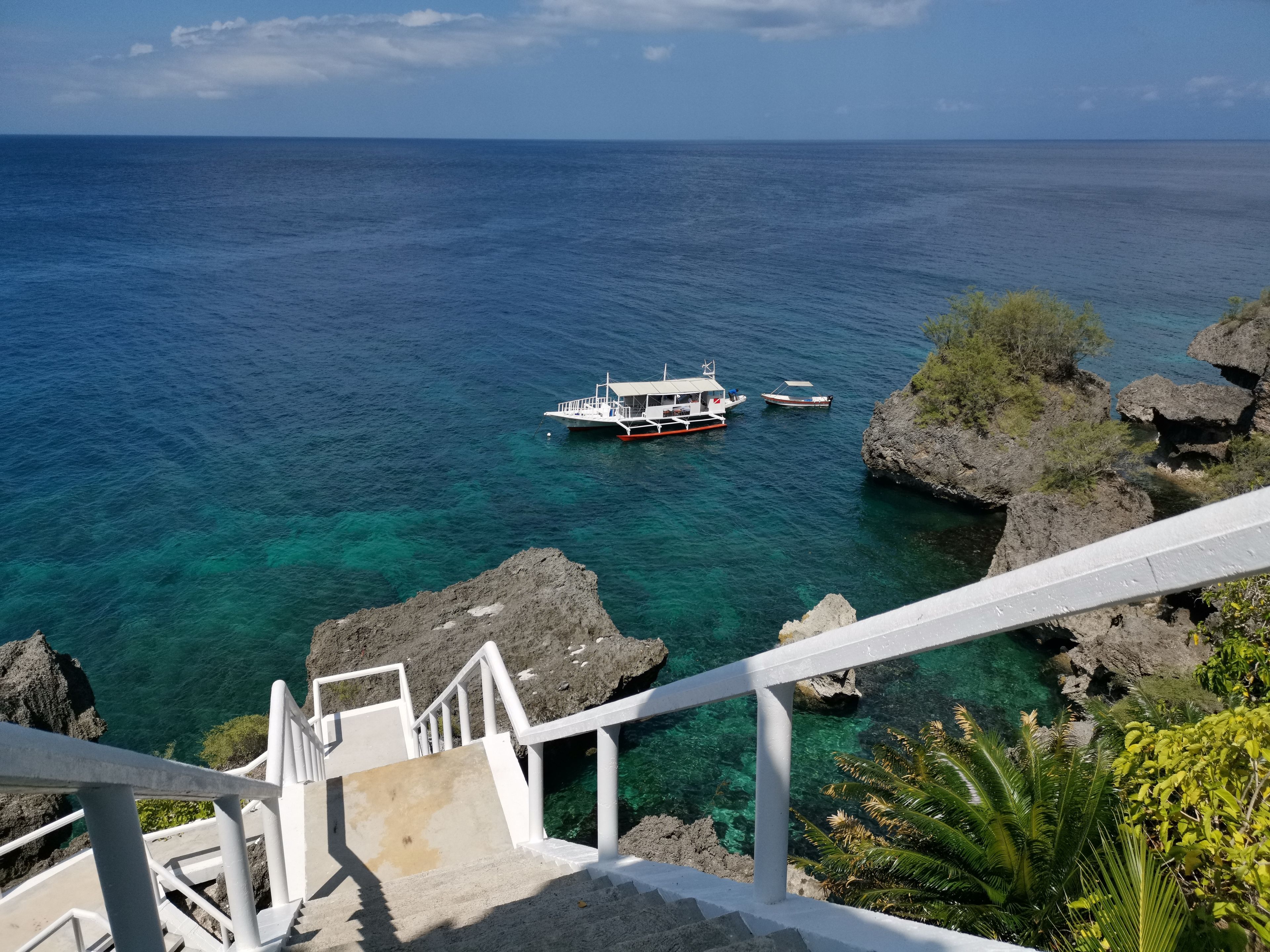 A staircase leading to a rocky coastline with clear blue sea and boats.