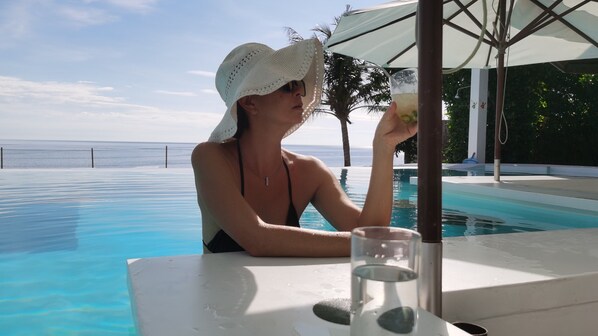 Uma pessoa sentada à beira da piscina, com vista para o oceano.