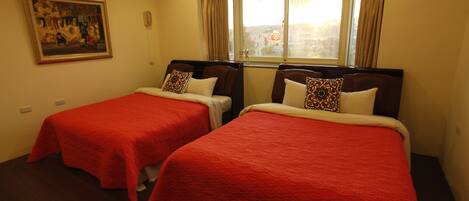 Habitación de hotel con dos camas, cada una con colcha y almohadas a juego. Hay un cuadro en la pared y una ventana con cortinas.