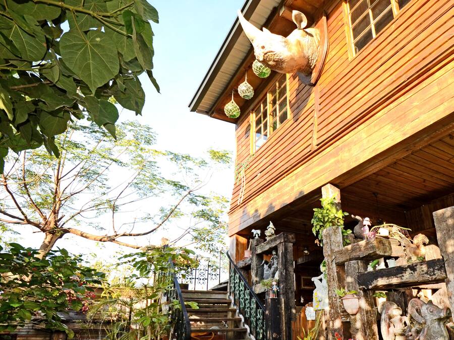Uma casa de madeira com escadaria que leva a um alpendre, decorada com vários enfeites e plantas.