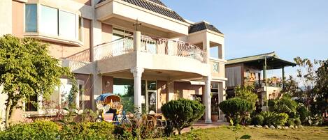 A two-story building with a balcony, a covered patio, and a well-maintained garden.