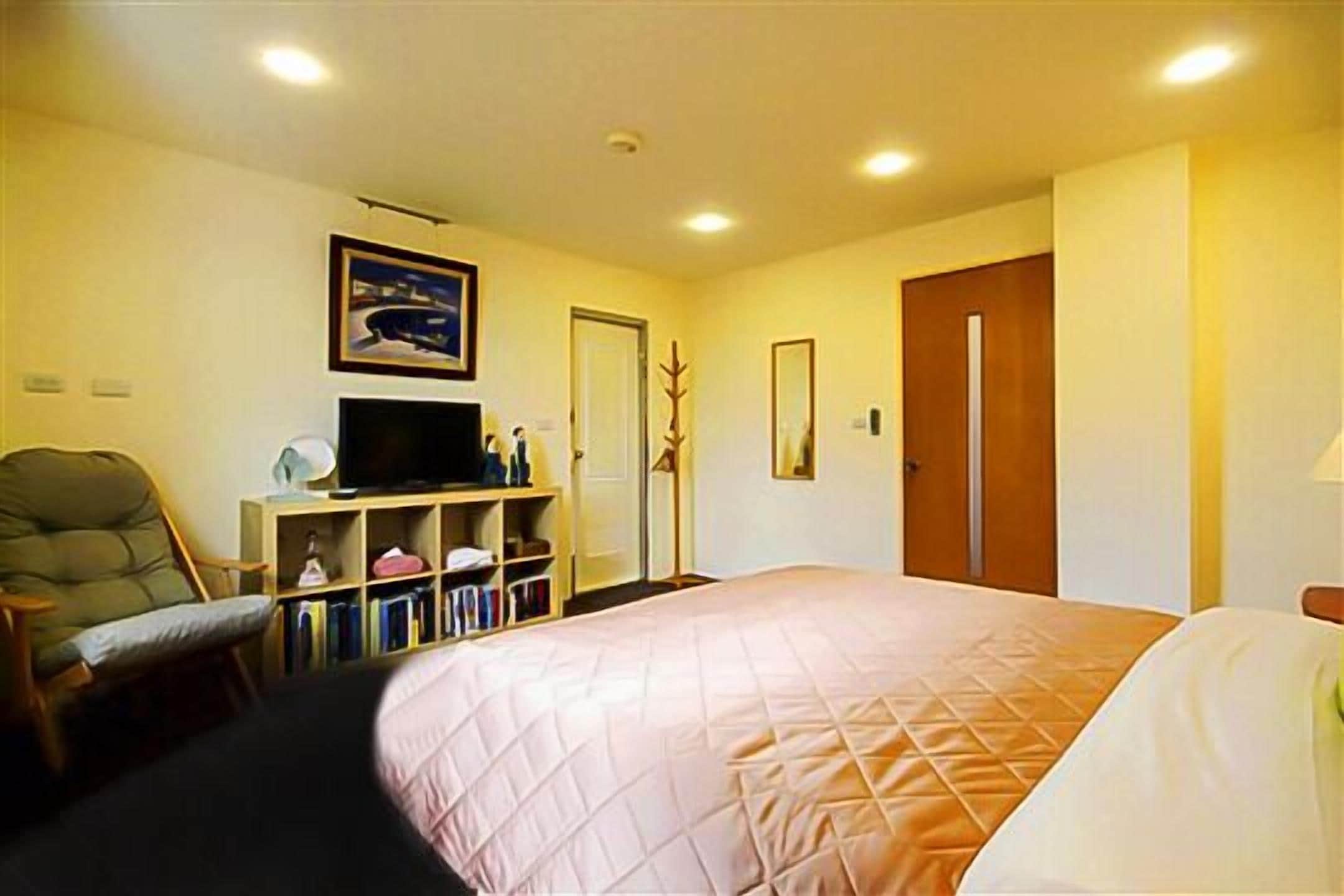 A hotel room with a bed, a television, a bookshelf, and a chair.