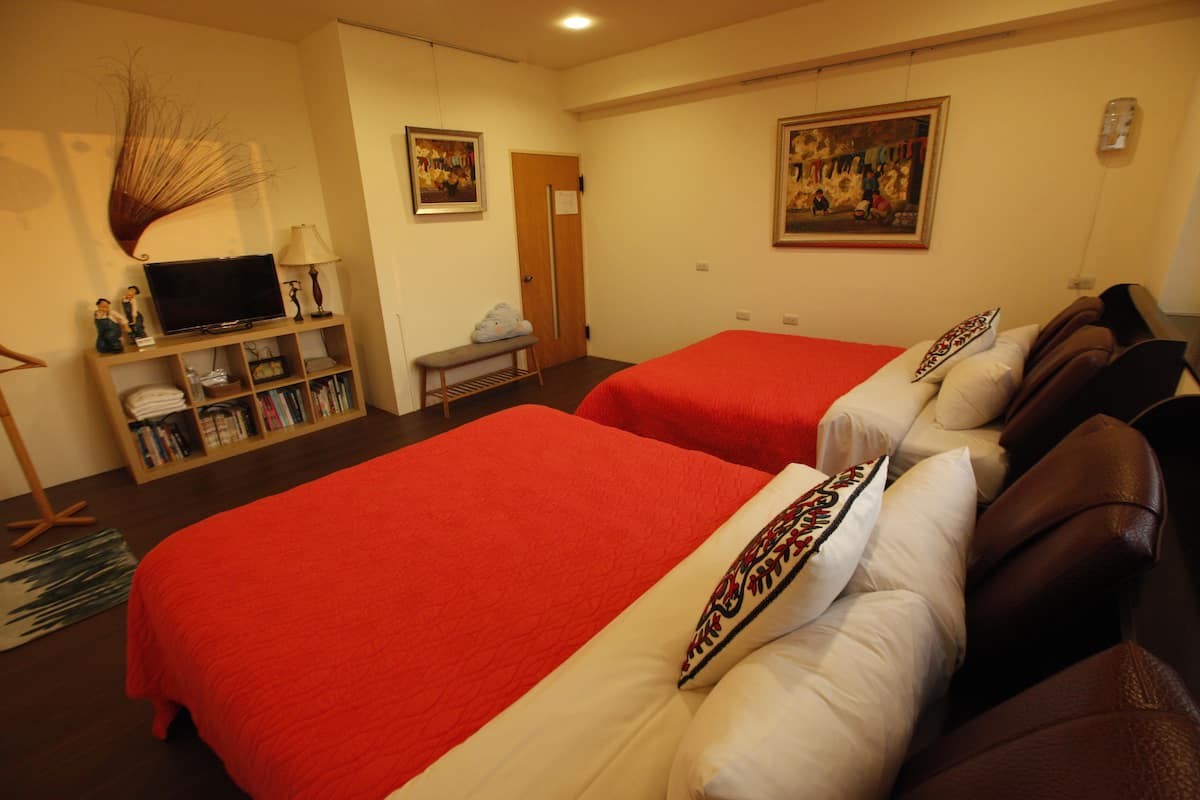 A hotel room with two beds, a TV, a bookshelf, and artwork on the walls.