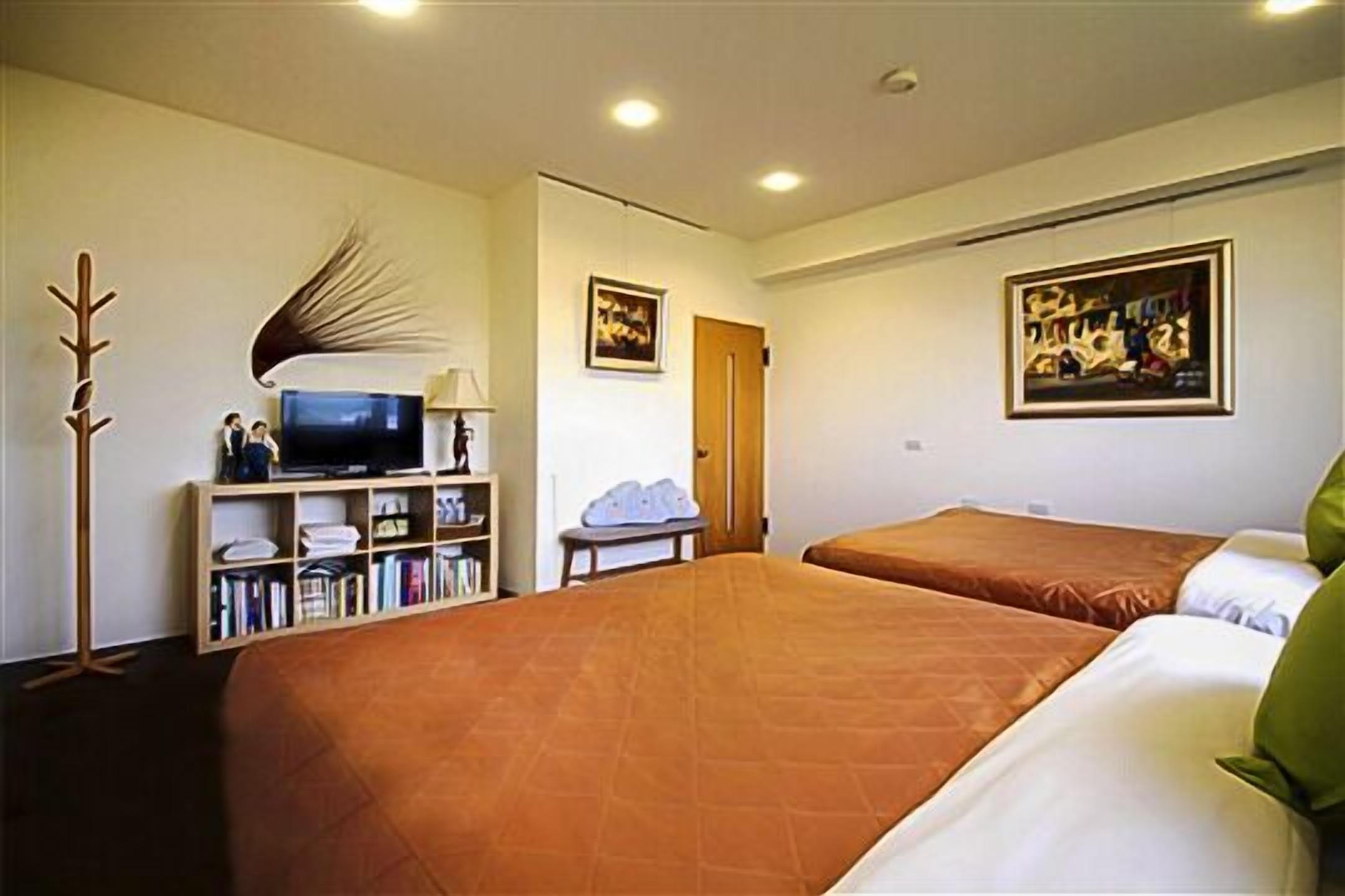 A hotel room with two beds, a television, a bookshelf, and artwork on the walls.