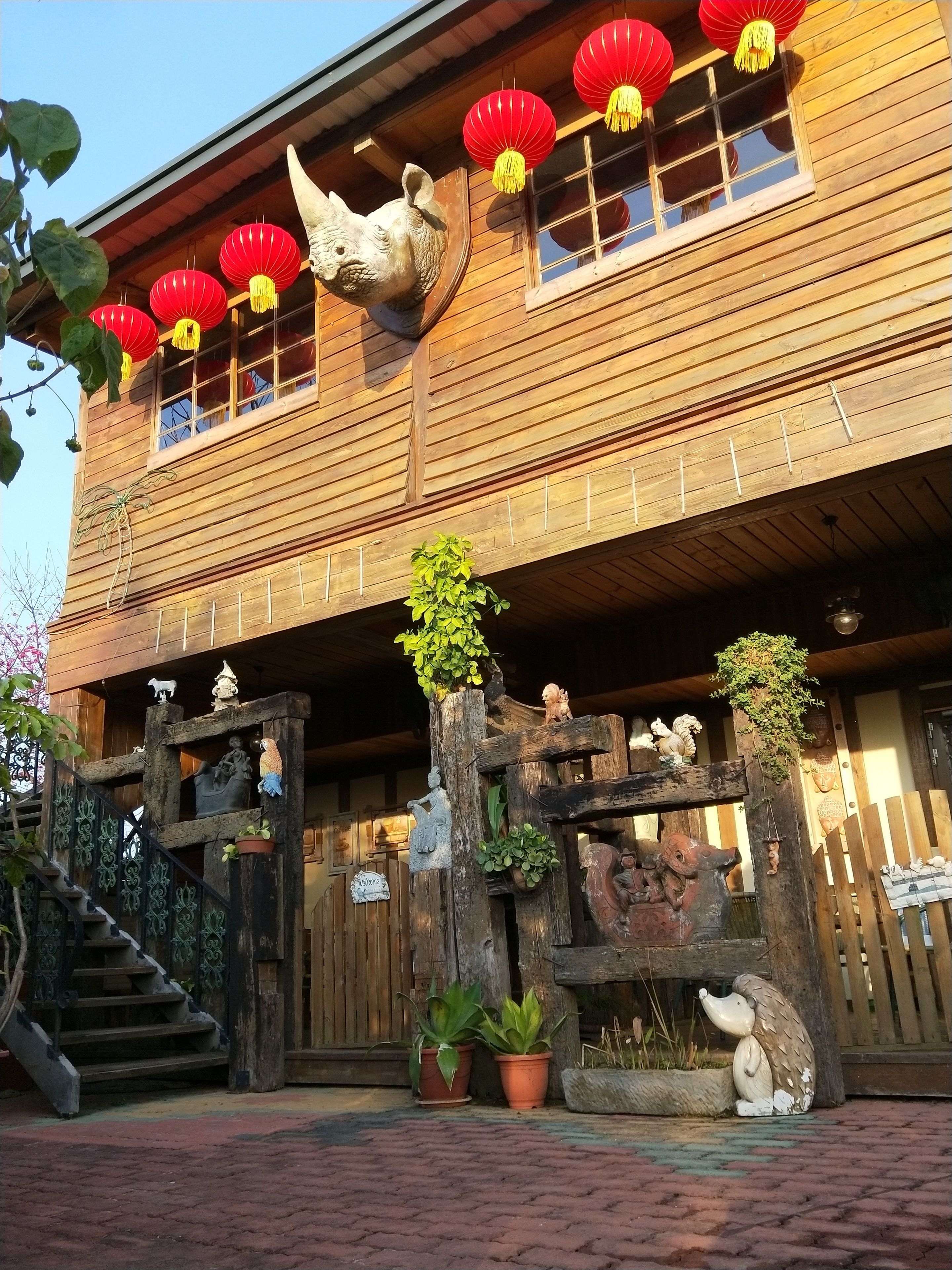 A wooden building with a traditional design, featuring a decorative wooden gate, potted plants, and a statue of a bird.