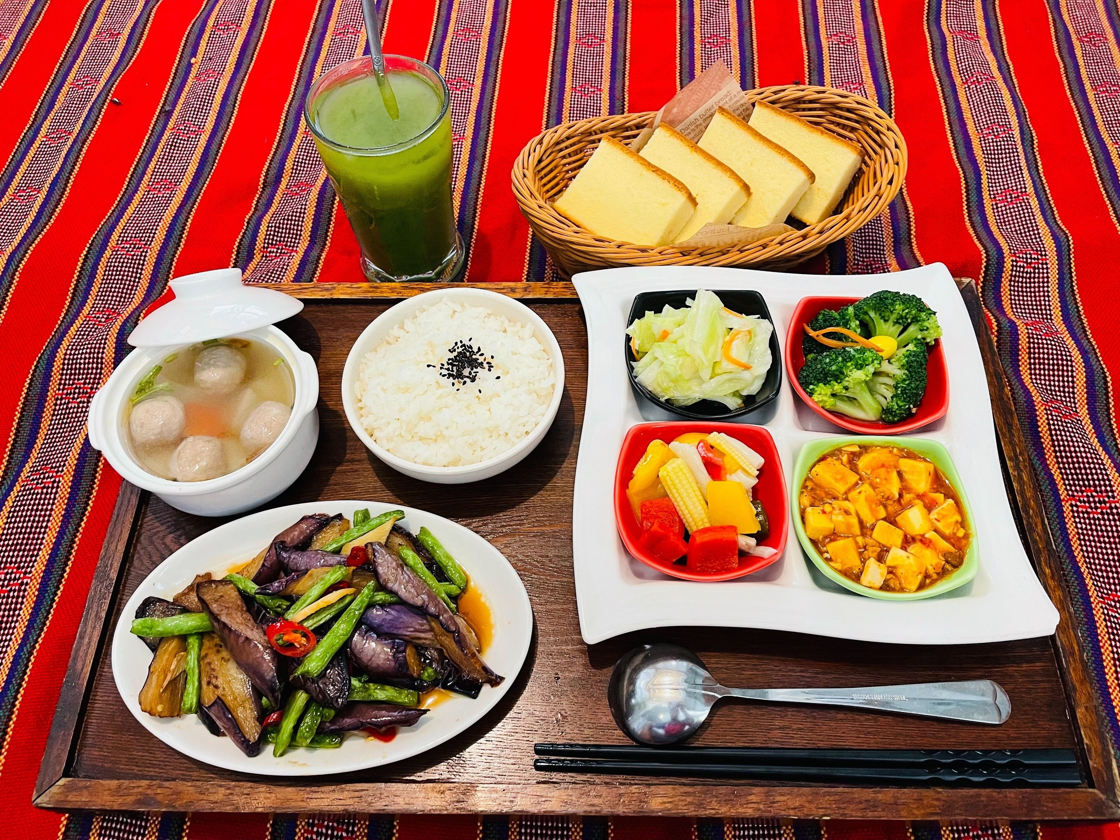 A meal tray with various dishes including meatballs in soup, rice, mixed vegetables, and a green drink.