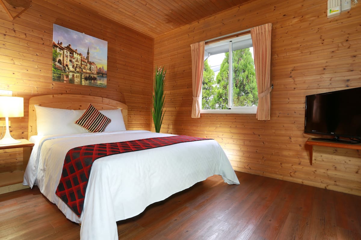 Una habitación con paneles de madera, una cama, un televisor y un ventanal con cortinas.
