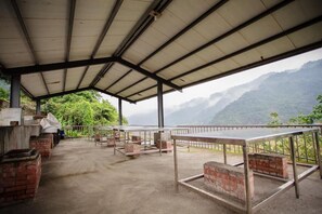 A covered outdoor area with tables and brick structures, overlooking a mountainous landscape. - Yingshih Resort (Datong)