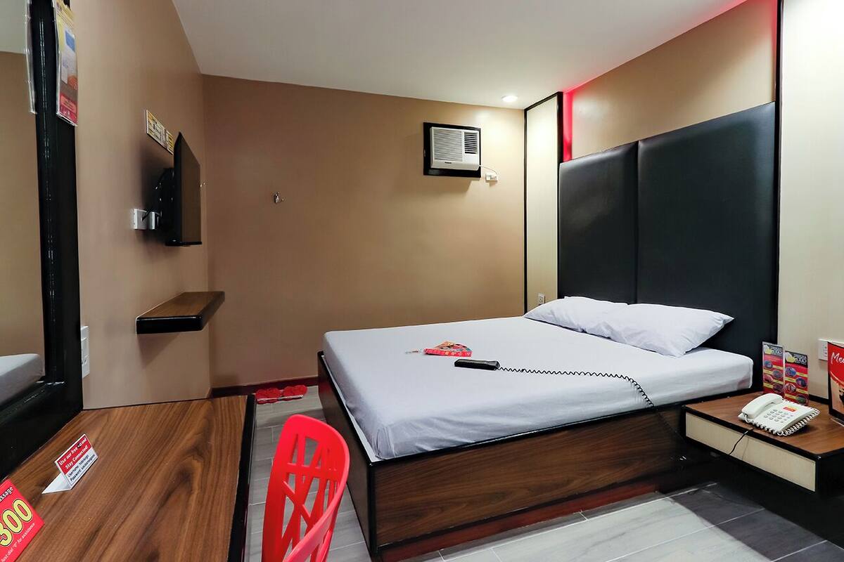 Una habitación de hotel con cama, mesita de noche, silla y un escritorio pequeño con teléfono.