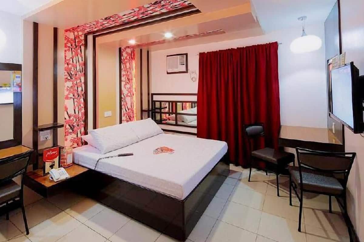 Habitación de hotel con cama, escritorio, silla, televisor y cortina roja.