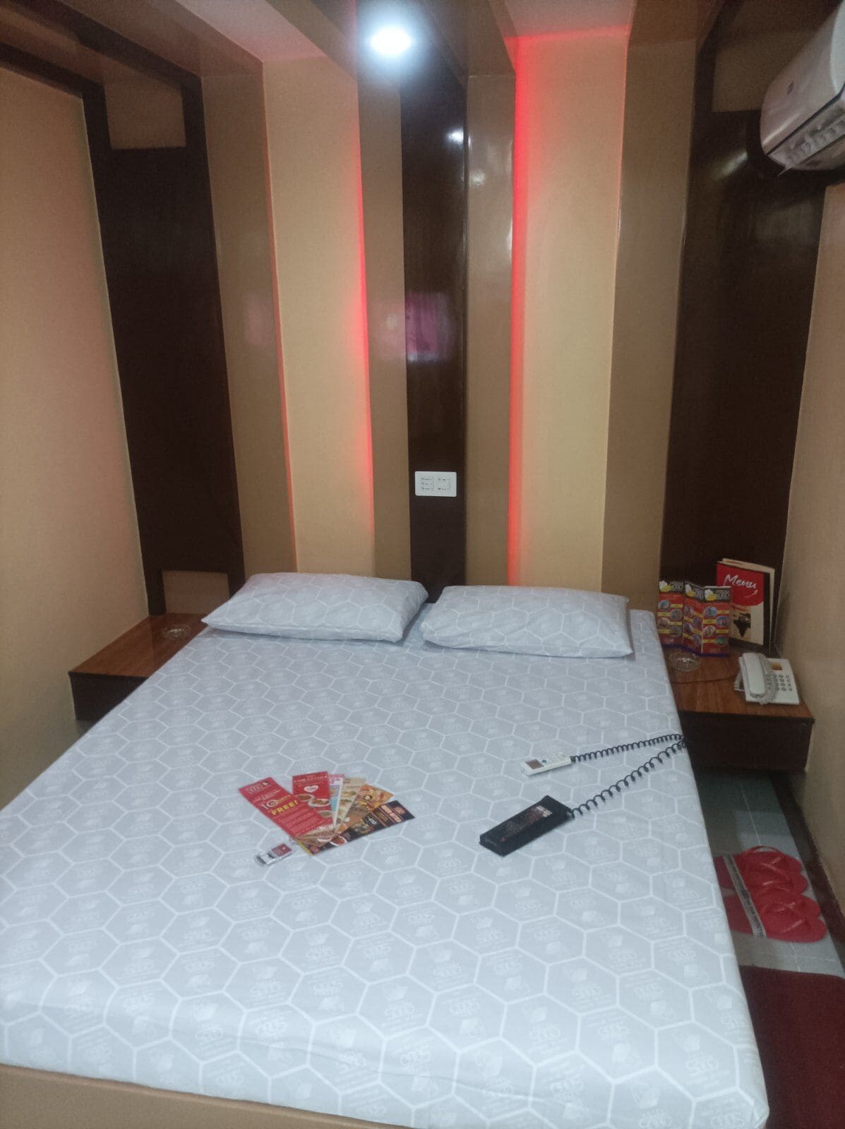 Ein Hotelzimmer mit einem Bett, zwei Kissen, einem Nachttisch mit Telefon und einer Wand-Klimaanlage.
