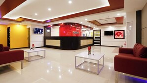 Un vestíbulo moderno con un mostrador de recepción, dos sofás rojos y un piso de baldosas limpias.