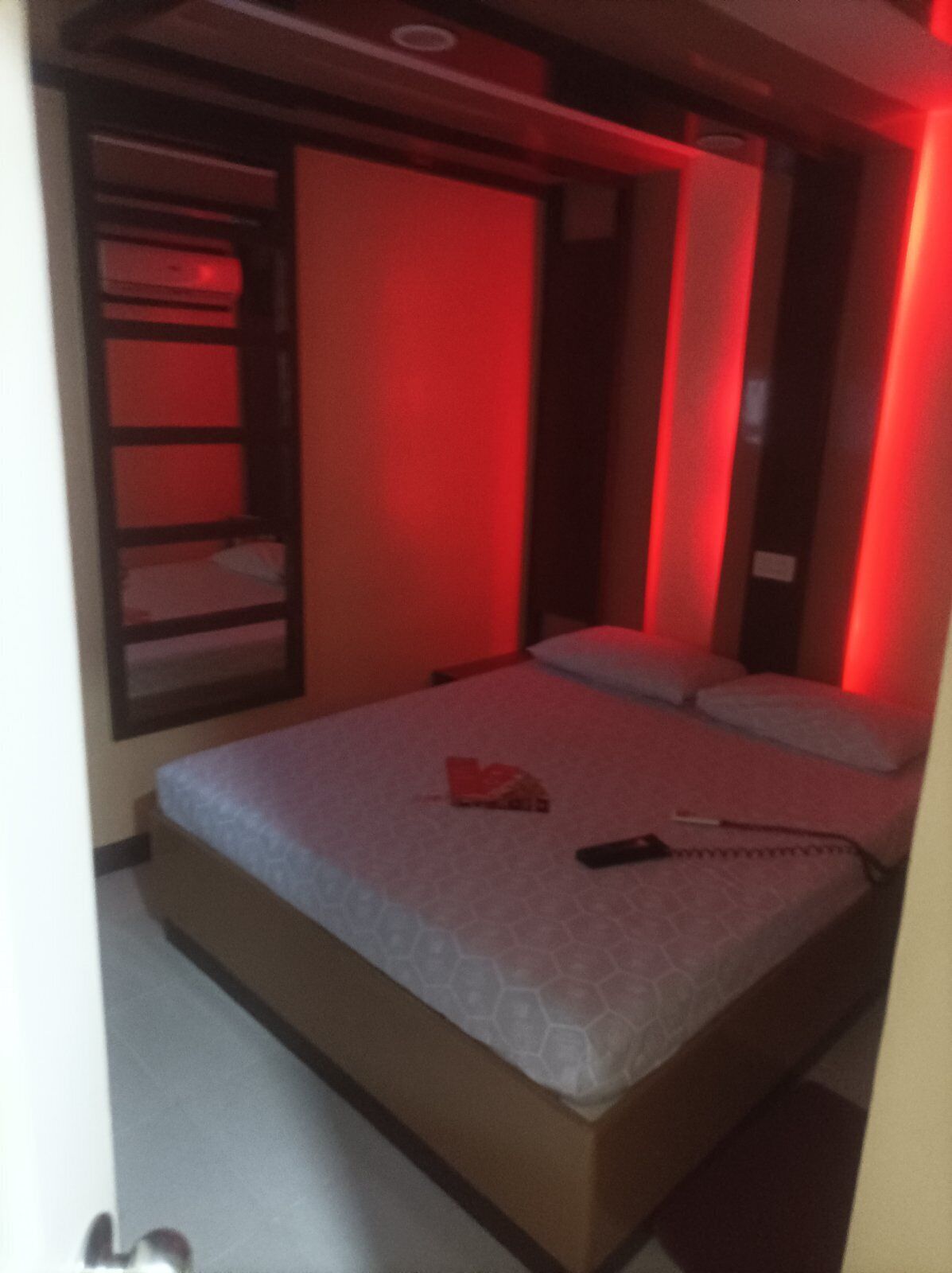 A room with a bed, a red-lit wall, and a built-in shelf.