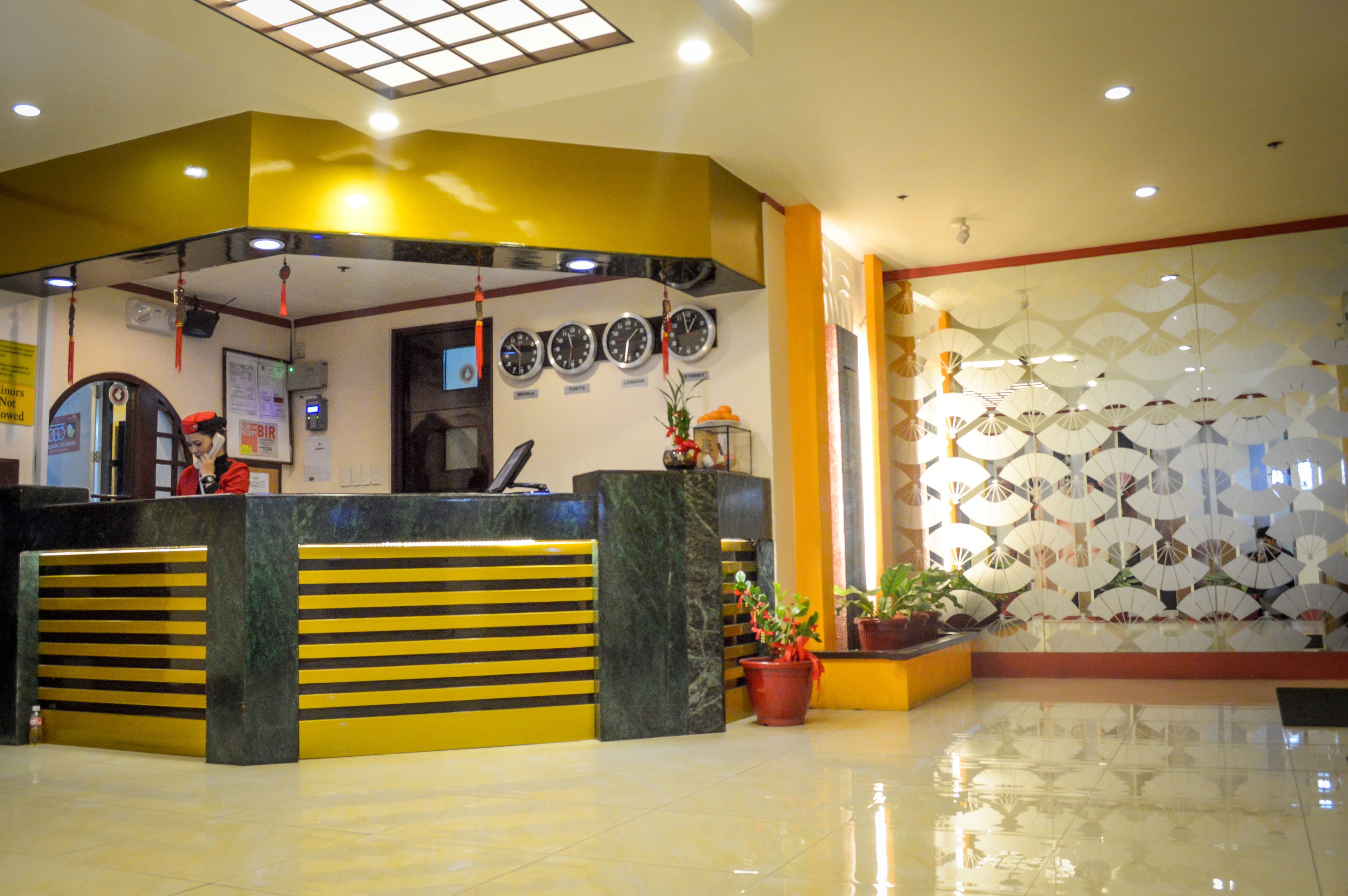 A hotel reception area with a counter, clocks, and decorative fans.