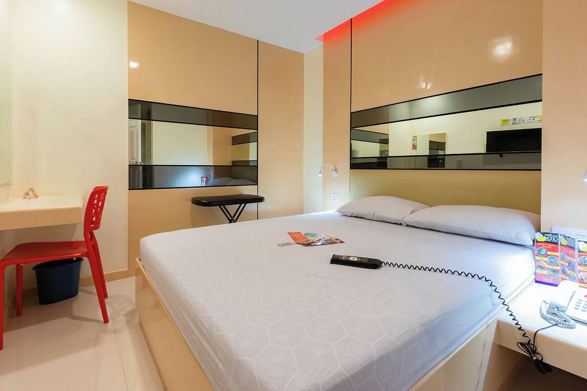 Habitación de hotel con una cama, un escritorio, una silla, un teléfono y un espejo.