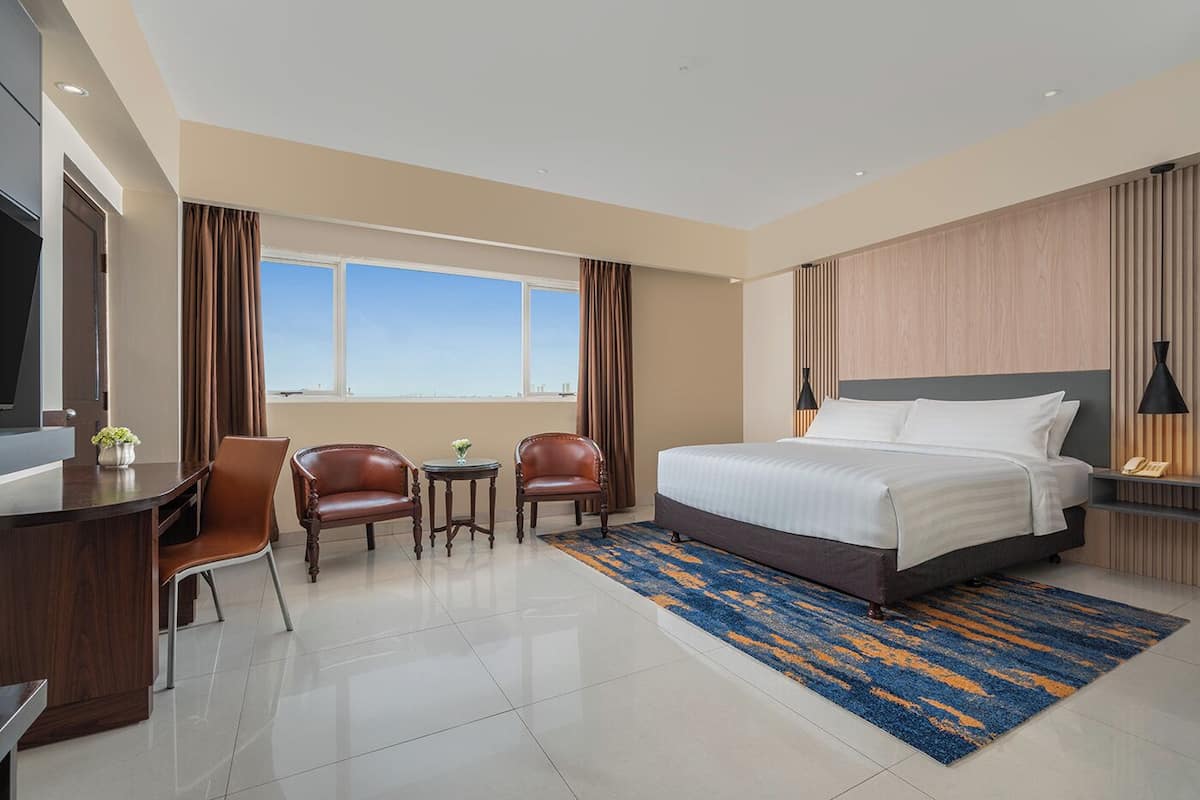 Una habitación de hotel con una cama grande, dos sillones, un escritorio y un televisor.