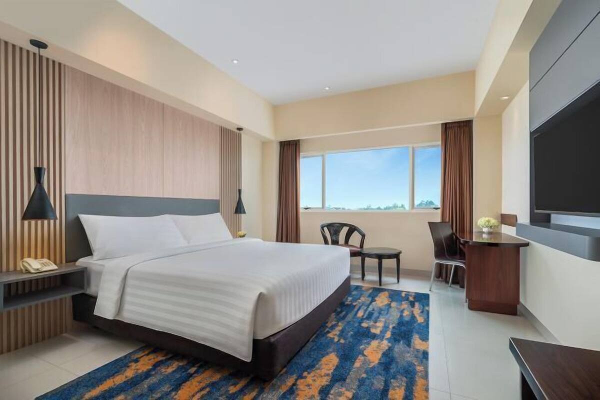 Habitación de hotel con cama, escritorio, silla, televisor y vistas al exterior.
