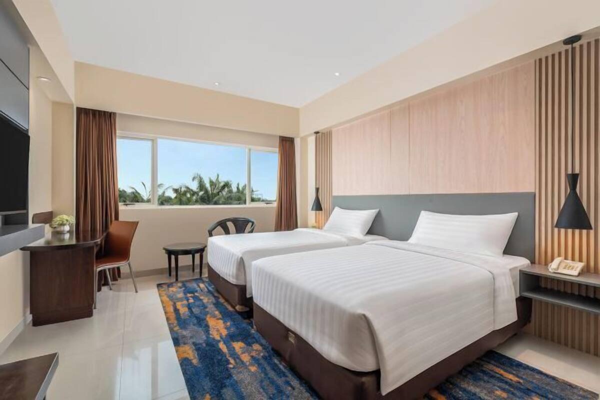 Habitación de hotel con dos camas, un escritorio, una silla, un televisor y una ventana con vistas.