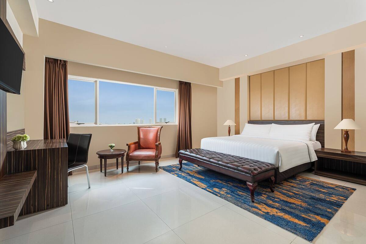 Habitación de hotel con cama, escritorio, silla, televisión y ventana con cortinas.