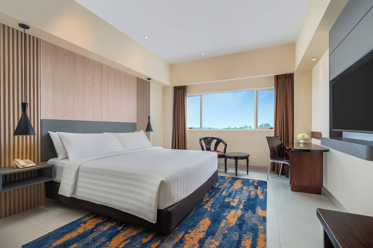 Una habitación de hotel moderna con una cama grande, un escritorio, una silla y un televisor.