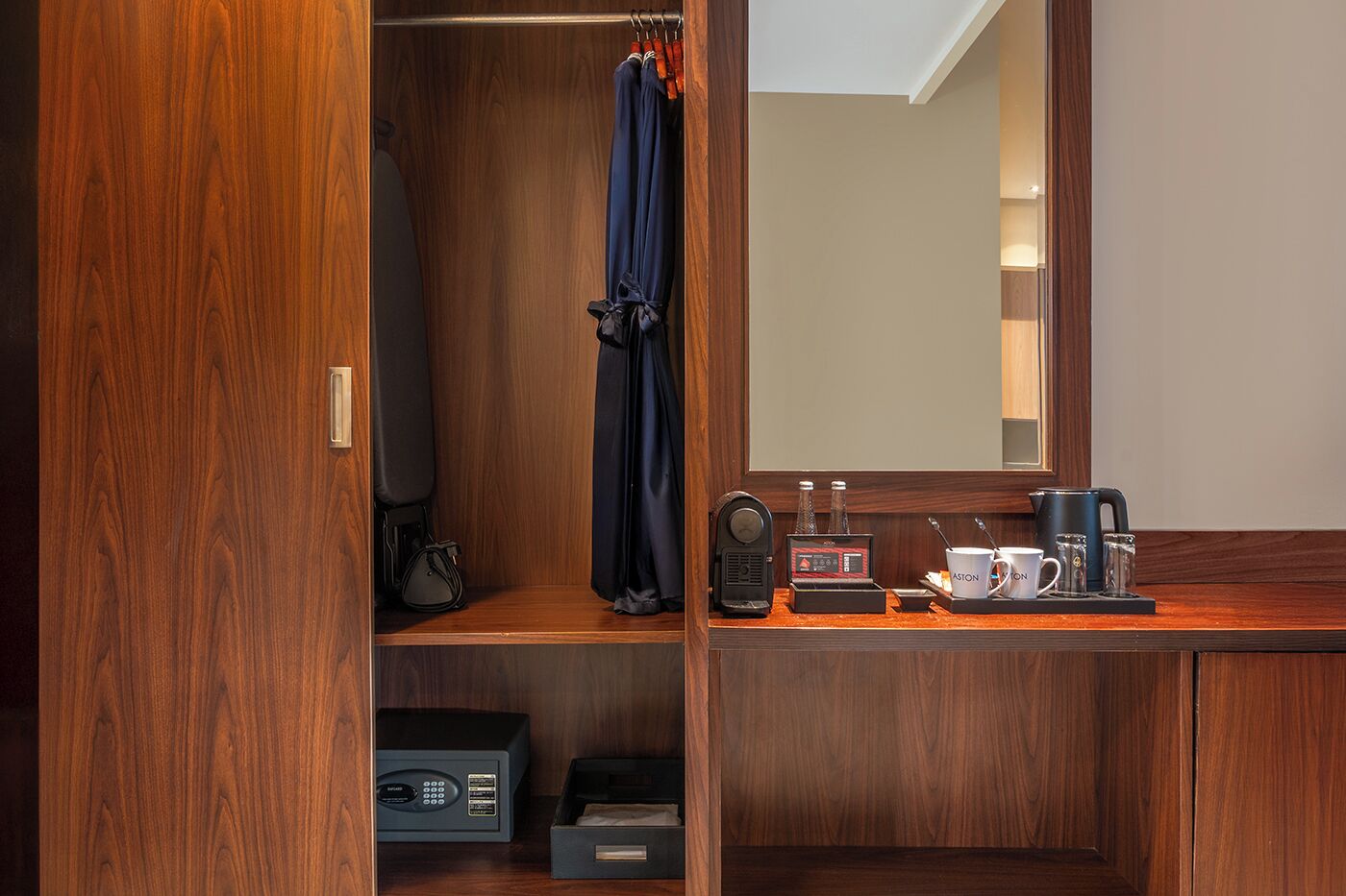 Habitación de hotel con un armario de madera, un espejo, una mesita con cafetera y un radio.