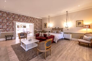 Une chambre bien éclairée, avec un lit, deux tables de chevet, une commode, un canapé rouge, une table basse blanche et deux fauteuils en osier.