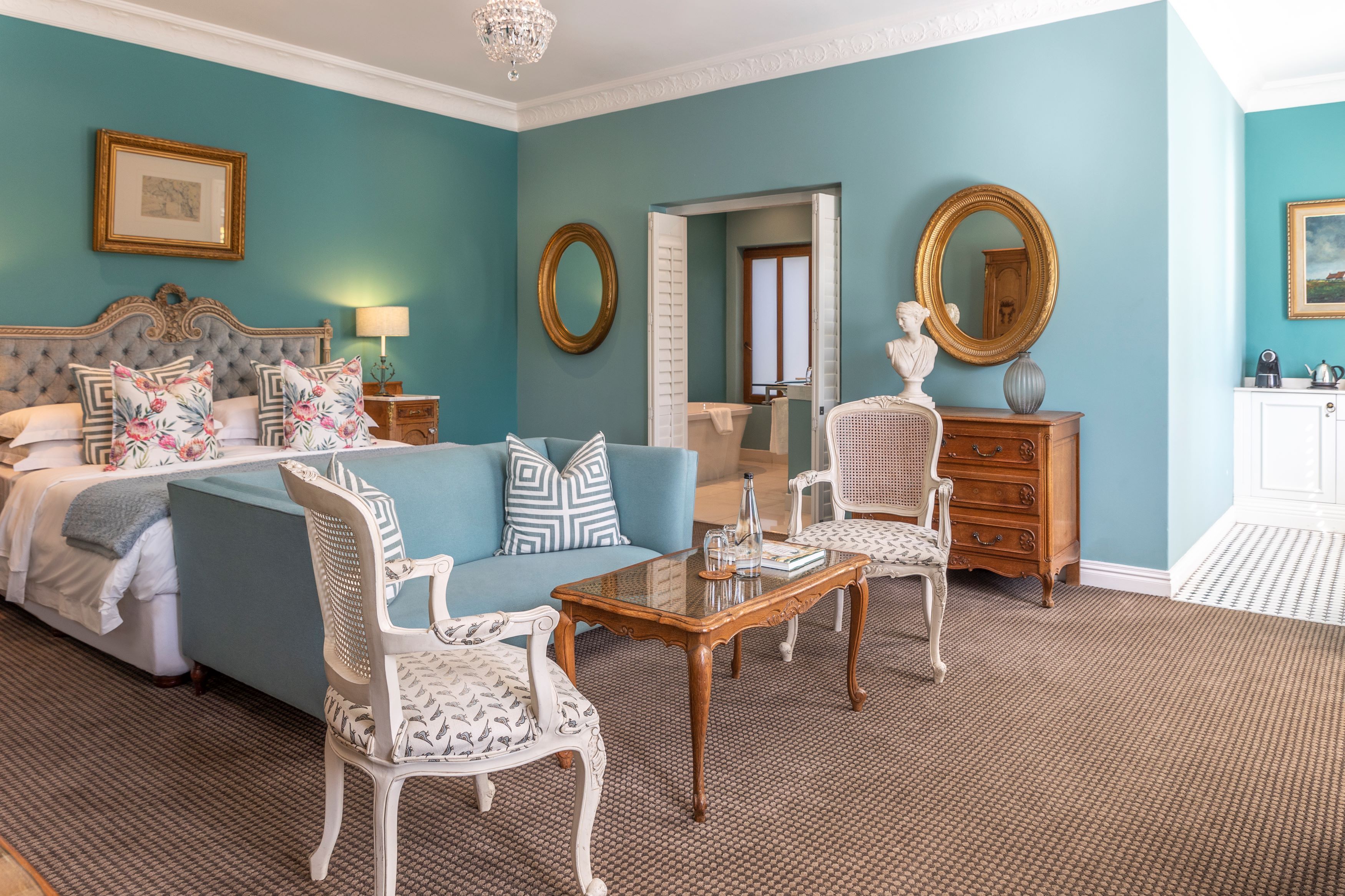 A hotel room with a bed, two chairs, a table, a dresser, and two mirrors.