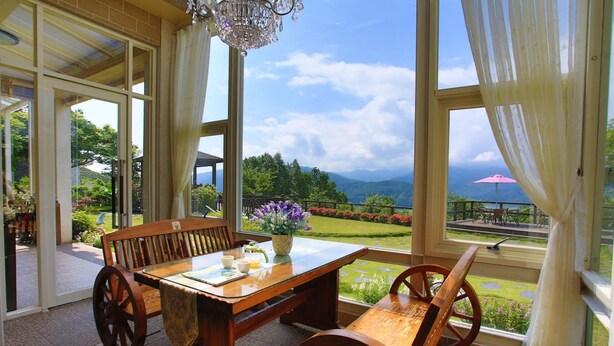 A wooden table and chairs in a sunlit room with large windows overlooking a garden and mountains. - Yilan Yalu Good View Homestay (Datong)