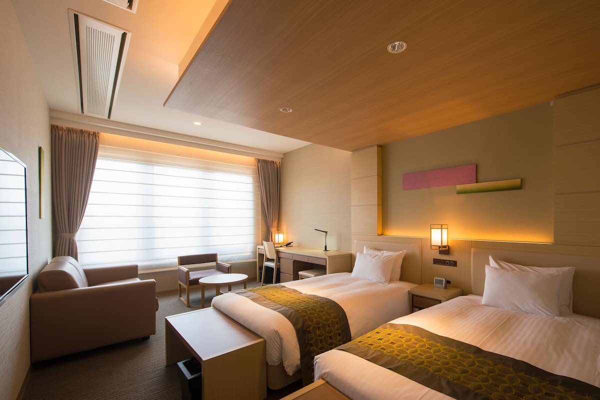 A hotel room with two beds, a desk, a chair, and a sofa.