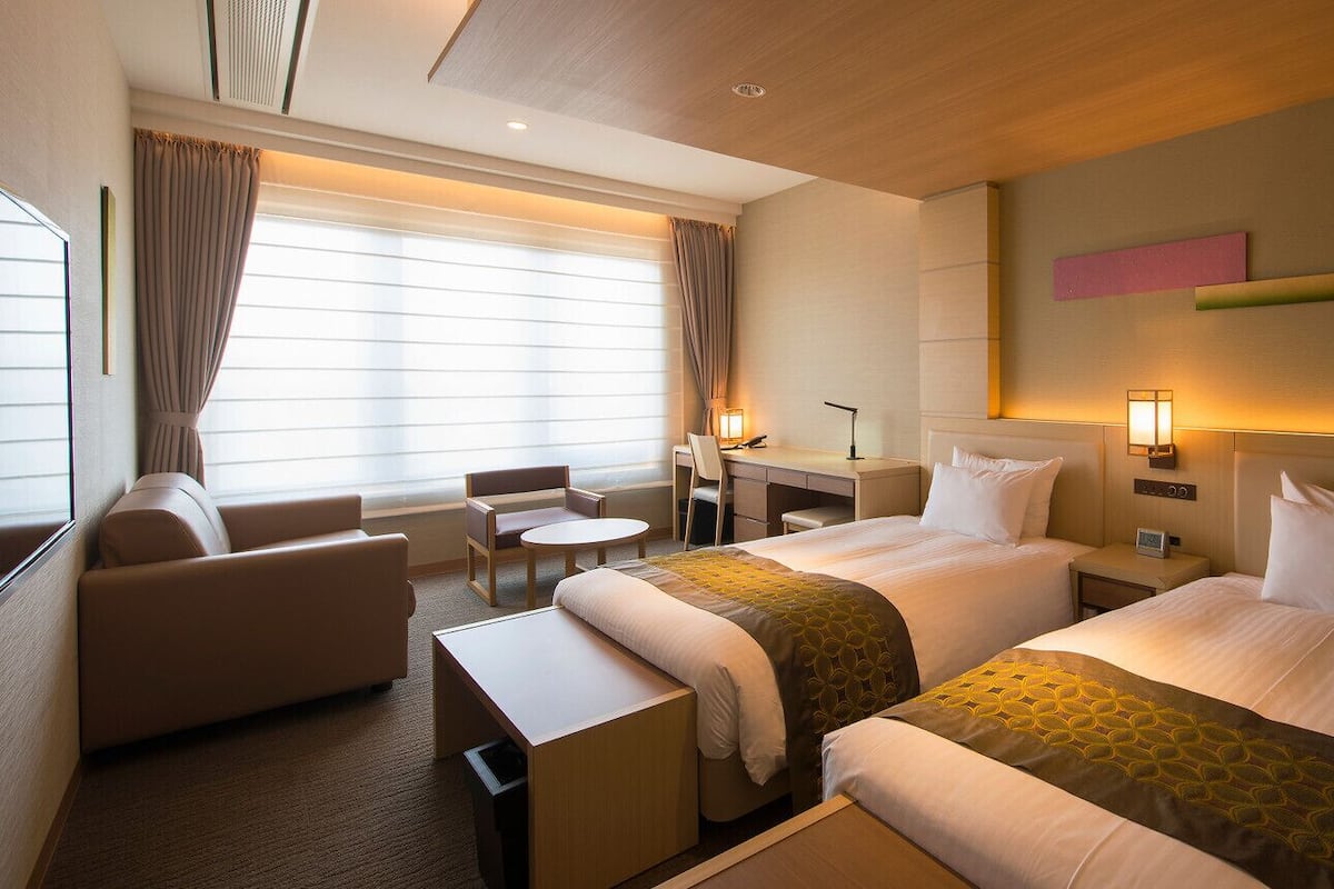 A hotel room with two beds, a desk, a chair, and a sofa.