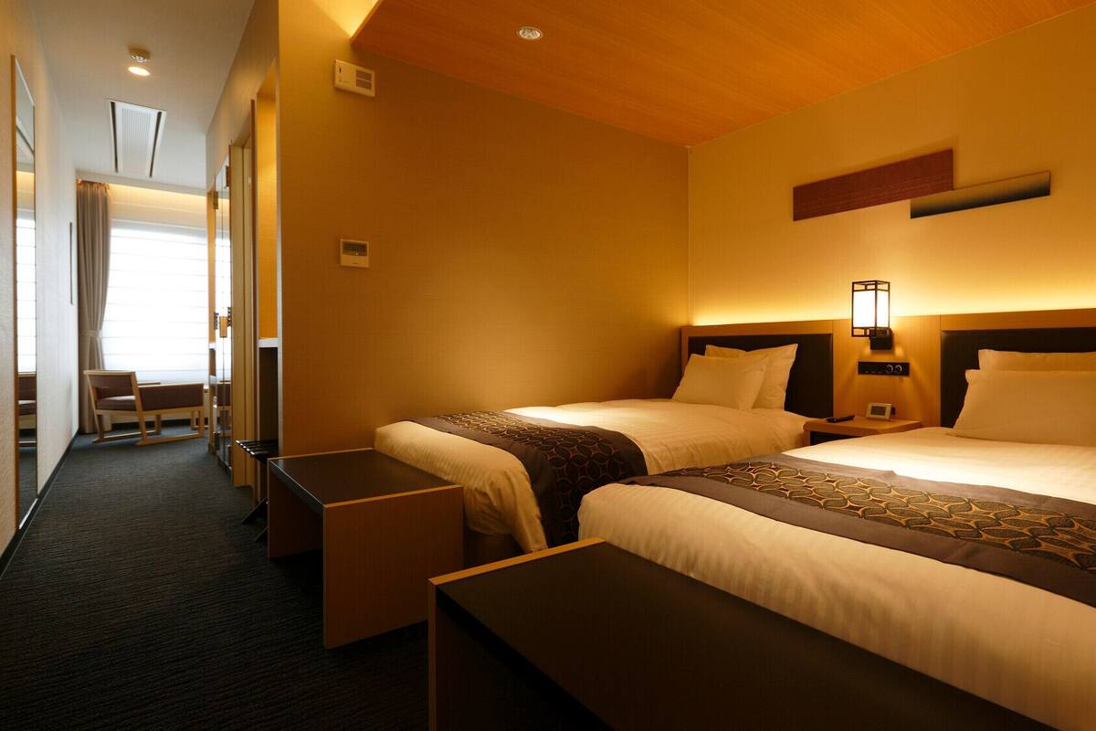 A hotel room with two beds, a desk, a chair, and a bedside table.