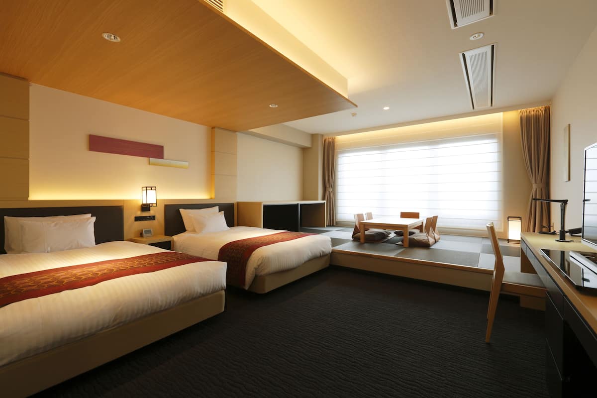 A hotel room with two beds, a desk, a chair, and a large window.