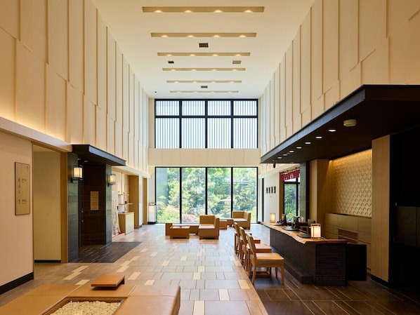 A spacious hotel lobby with a high ceiling, large windows, and a central seating area.