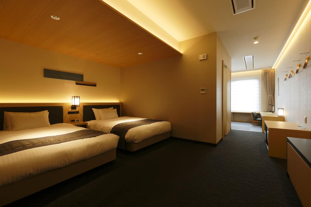 A hotel room with two beds, a desk, and a chair.