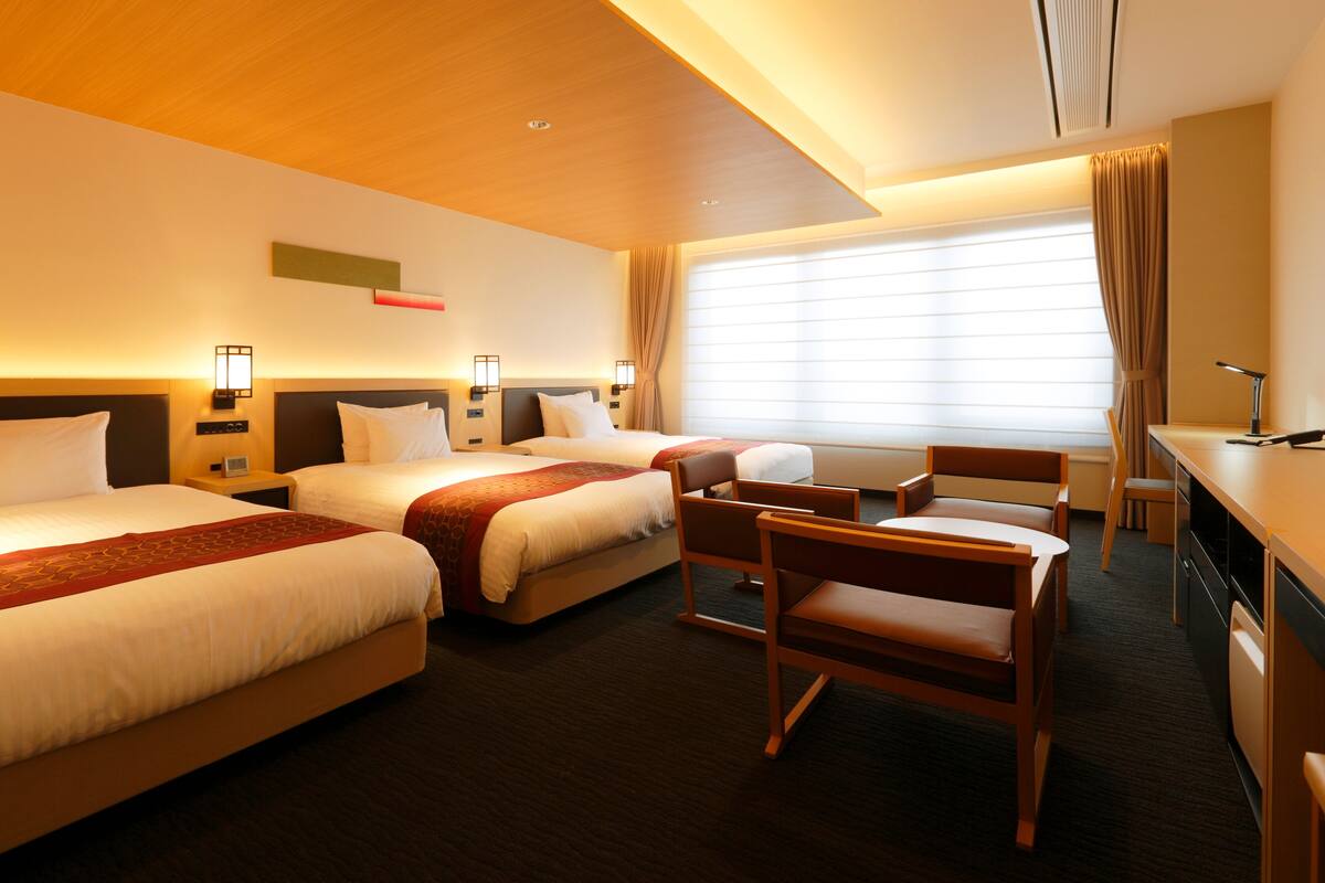 A hotel room with two beds, a desk, and a chair.