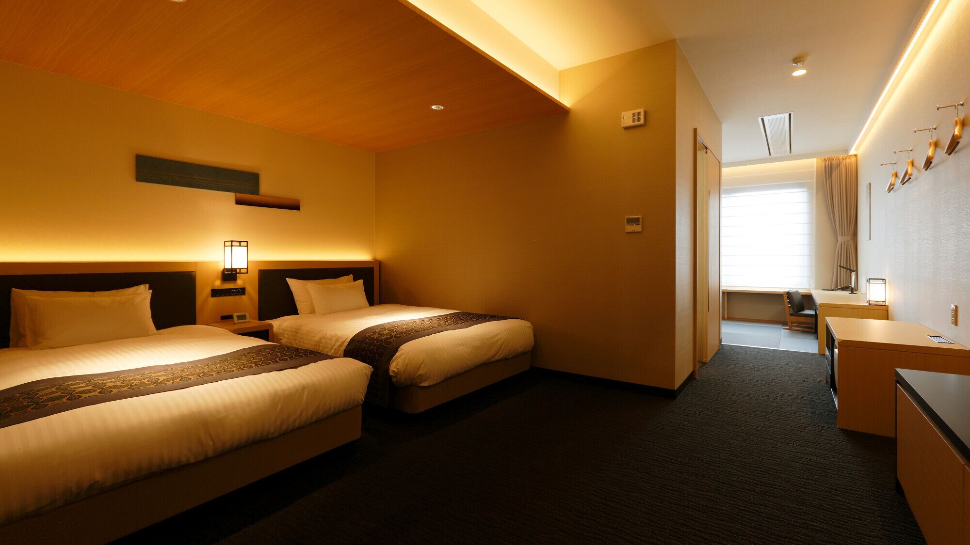 Habitación de hotel con dos camas, un escritorio, una silla, ventana con cortinas y aire acondicionado instalado en la pared.