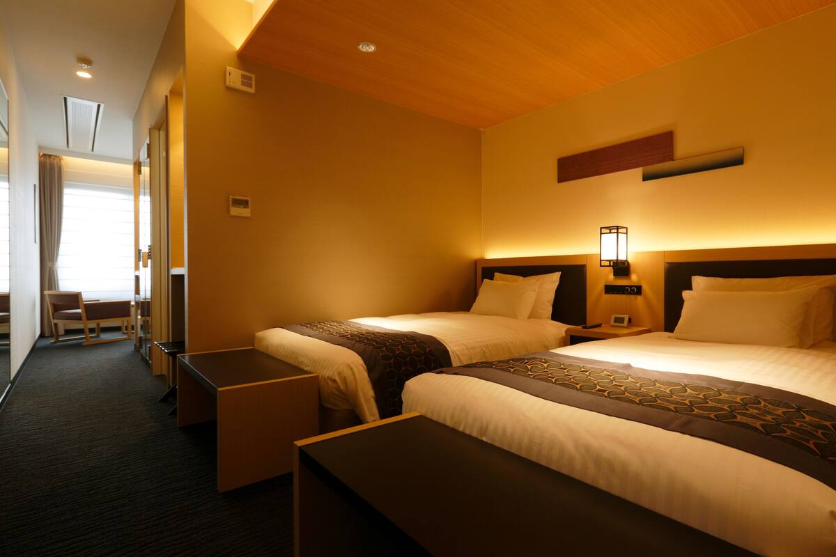 A hotel room with two beds, a desk, and a chair.