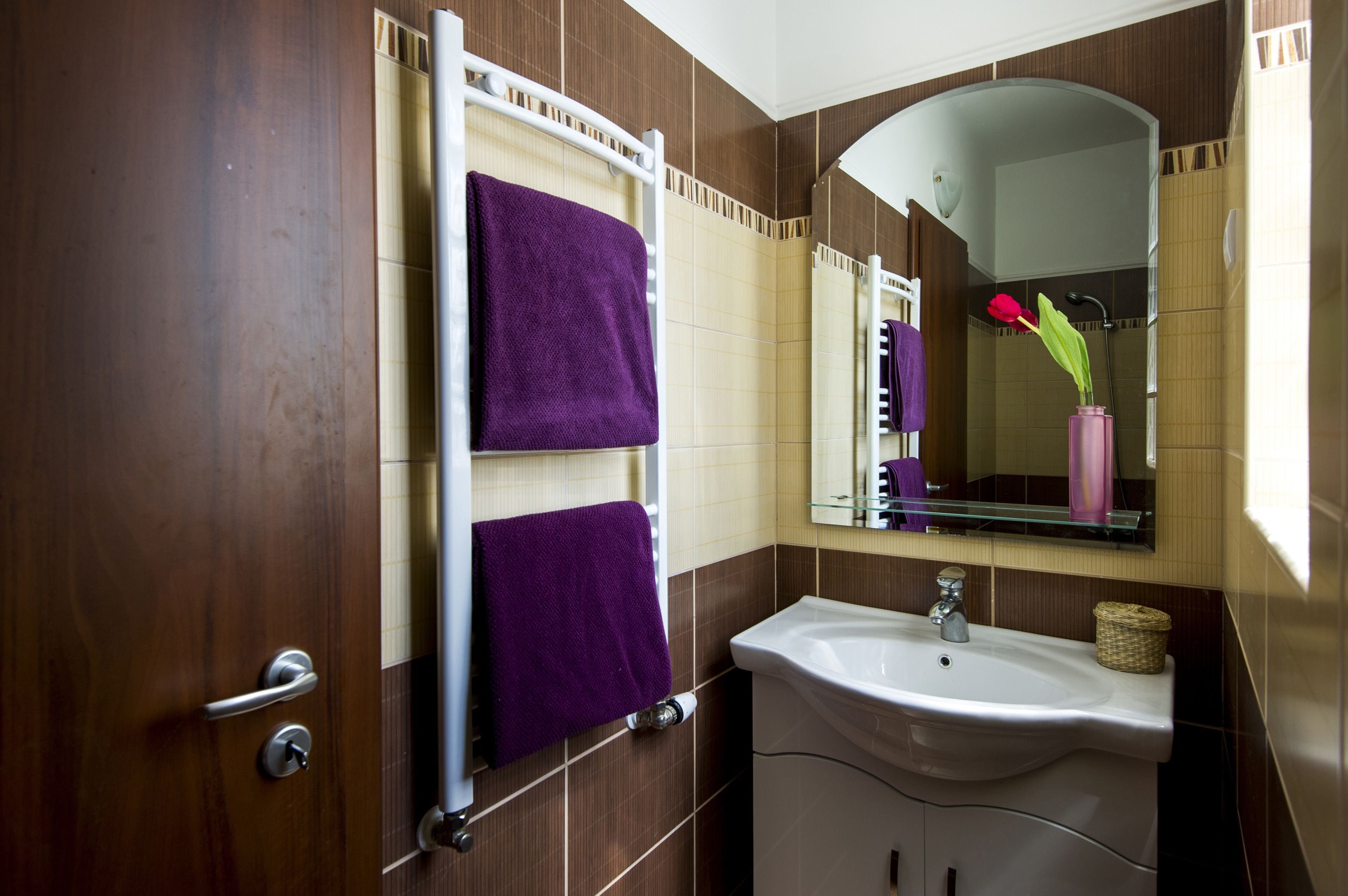 A bathroom with a wooden door, a white sink, and a mirror reflecting a red flower vase.