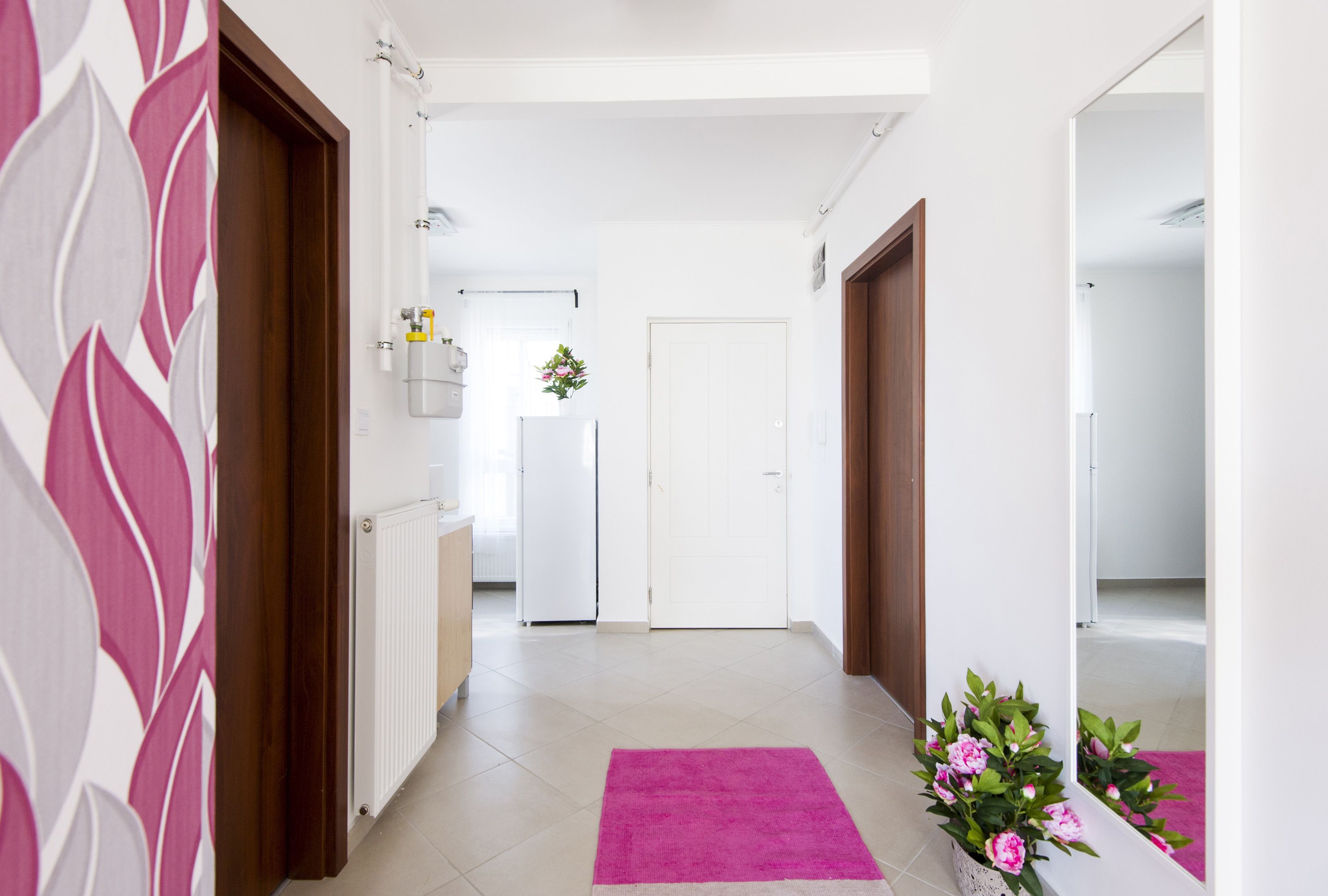 Un pasillo con un tapete rosa, una puerta blanca y una planta con flores rosadas.