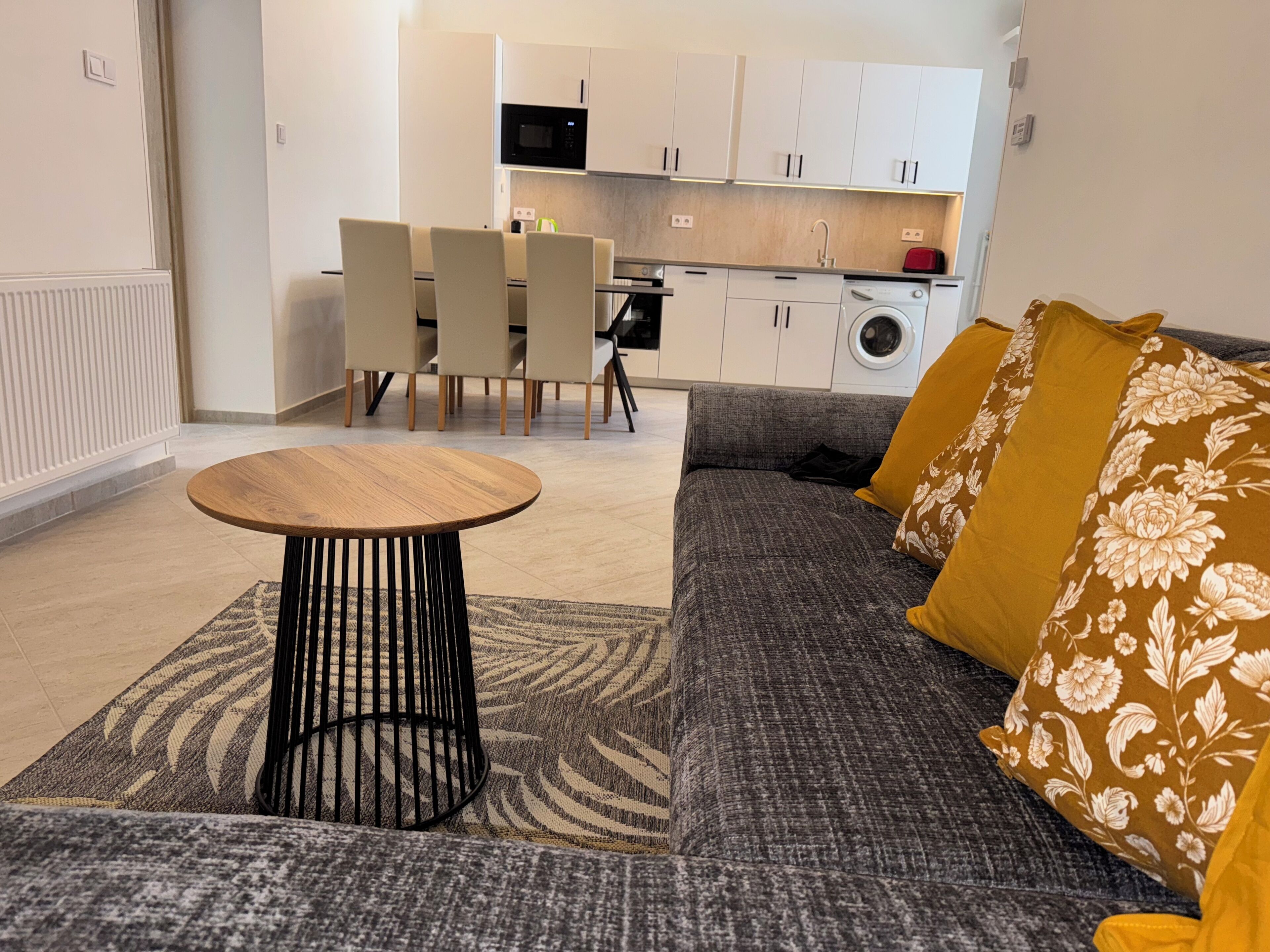 A modern living room with a grey sofa, a round wooden coffee table, and a patterned rug.