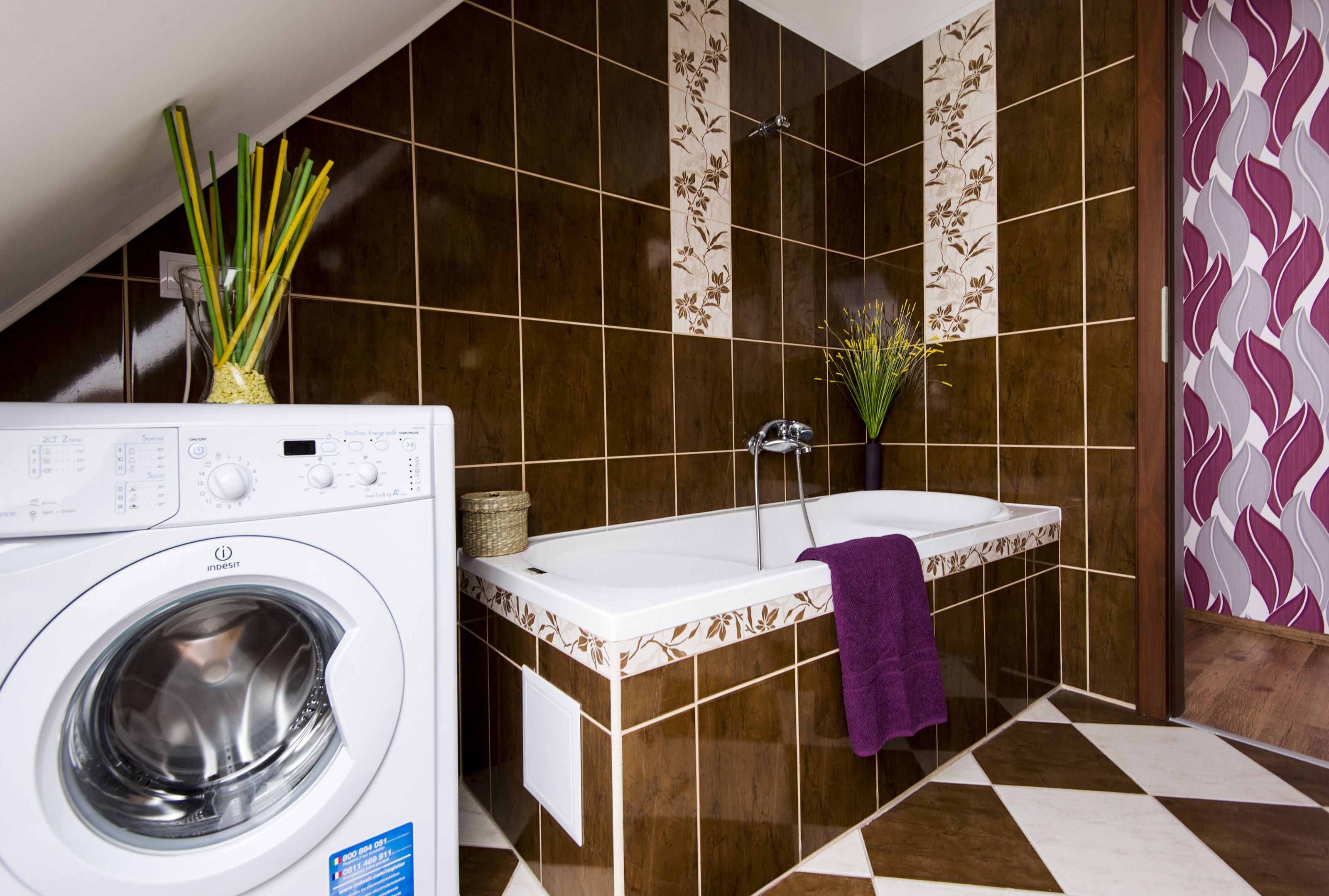 Un espace buanderie avec un lave-linge et une baignoire, ainsi qu’une serviette violette.