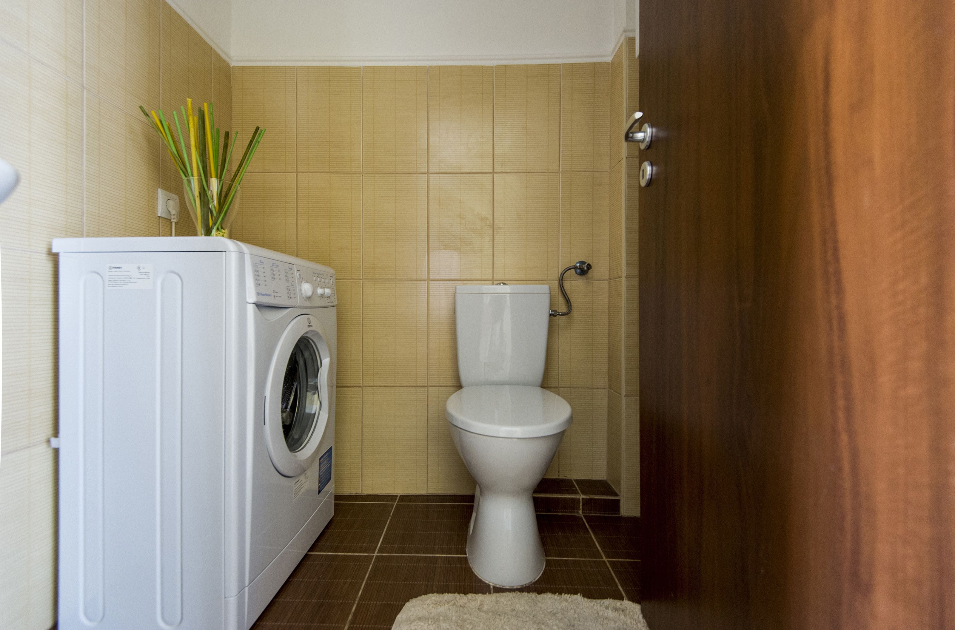 A compact bathroom with a washing machine, toilet, and a wooden door.
