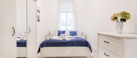 A bedroom with a bed, a dresser, a mirror, a window, and a vase with flowers.