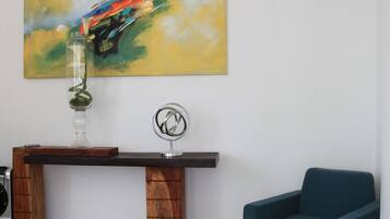 Una sala de estar moderna con una mesa consola de madera, un florero con una planta verde, un sillón azul y un cuadro abstracto colorido en la pared.