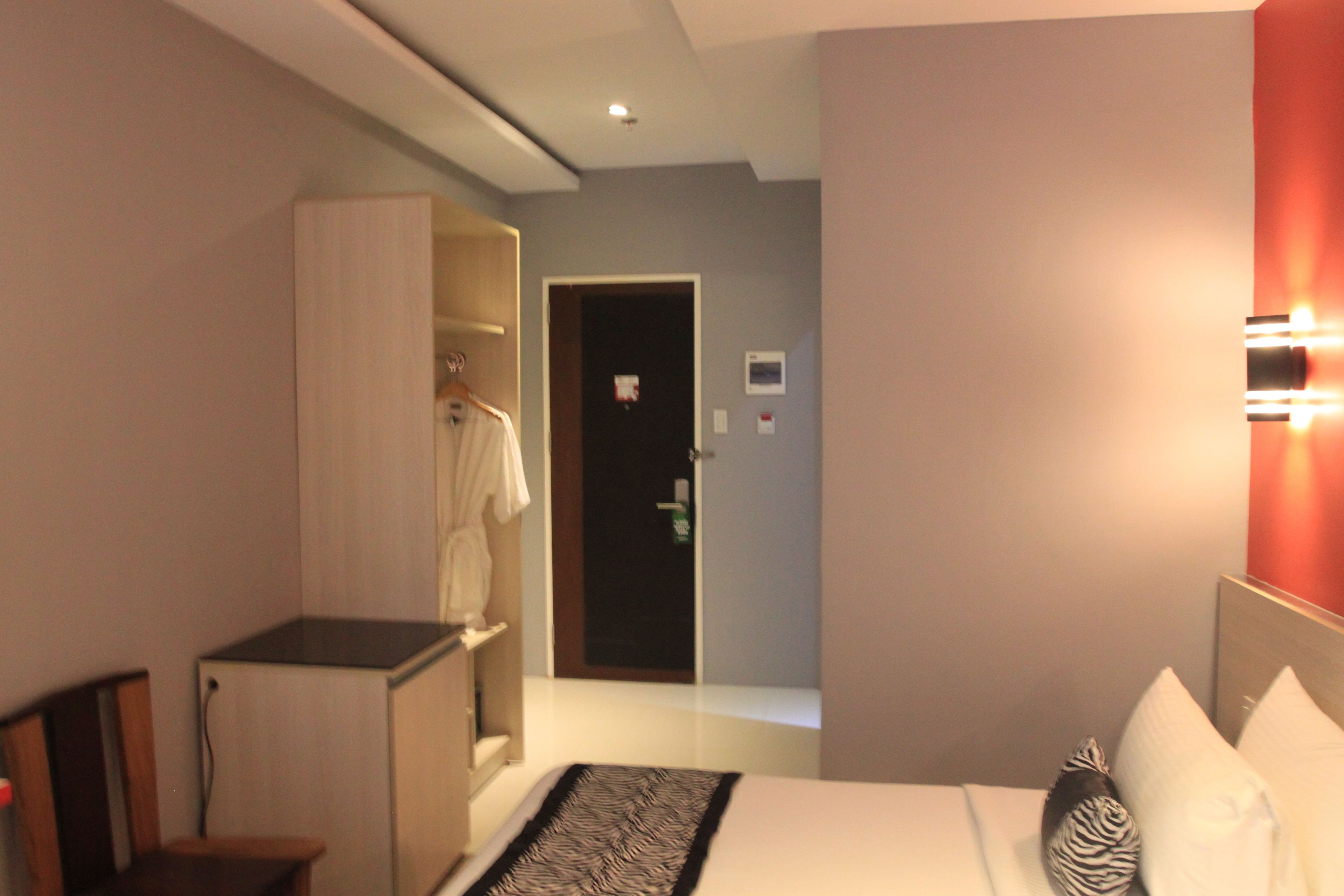 A hotel room with a bed, a desk, a wardrobe, and a door leading to another room.