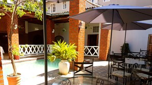 An outdoor patio with a glass table and chairs, surrounded by brick walls and a pool. - The Lusaka Hotel (Lusaka)