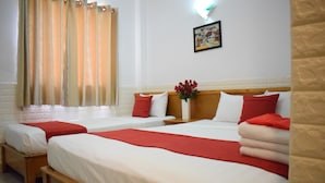 A hotel room with two single beds, each with a red and white pillow, and a wooden headboard. There is a window with curtains, a wall-mounted picture, and a vase with red flowers on the nightstand. - Marie-Line Hotel (Ho Chi Minh City)
